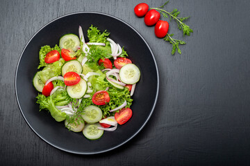 Healthy vegetable salad in black bowl on wood background.