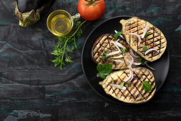 Grilled eggplants in plate on black wood background.