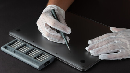 The master repairs a laptop in white gloves with a screwdriver and a set of bits