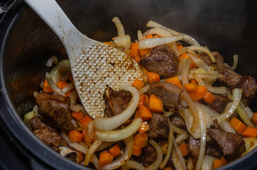 The cook fries pieces of lamb meat with onions and carrots in a saucepan to prepare pilaf