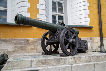 A bronze cannon on a carriage located on a white stone pedestal near the arsenal building in the...