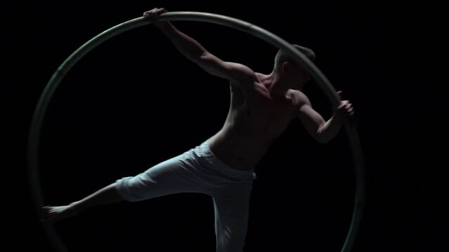 Muscular circus artist perform Cyr Wheel on a black background stage in slow motion
