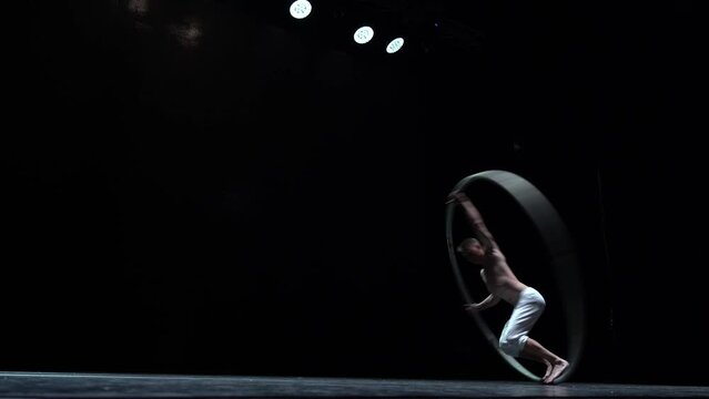 Muscular circus artist perform Cyr Wheel on a black background. Concept of Individuality and creativity 