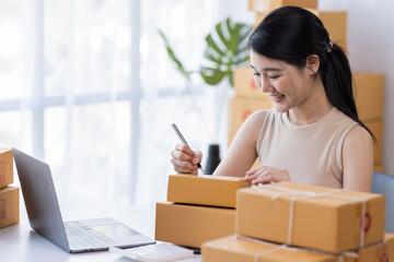 Obraz na płótnie Canvas SME entrepreneur Business Young Asian freelance girl works with a laptop and box at home, about eCommerce, business, seller, Asian, employee, entrepreneur, box, merchant, Online SME business ideas,