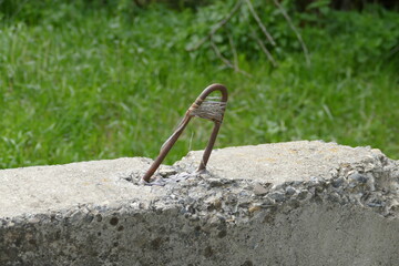 Bent rusty metal wire stuck in concrete, with nature in the background.