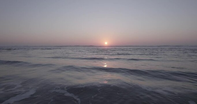 Aerial dolly shot over the sea towards the setting sun in the horizon