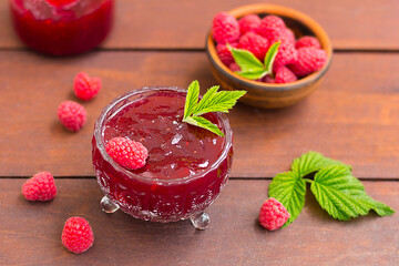 fresh raspberry jam in a glass jar on a wooden table, next to fresh raspberries. concept of homemade jam, preserves for winter, selective focus