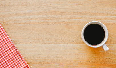Flat lay view of black coffee in white ceramic cup on classic pink tablecloth and wood table with copy space