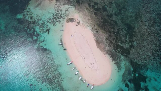 Drone shot of a sandy land in turquoise water with moored kayaks with outriggers in Philippines