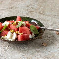 a bowl of watermelon with feta cheese and pistachios on a light table