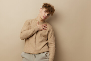 a charming man in a beige sweater stands on a beige background and it's nice to look into the camera with his hand on his body