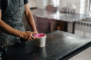 Fototapeta na wymiar Artisan sculptor artist mixing paint in his workshop. Pink paint, paint mixer