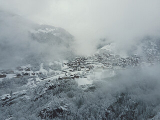 Skiing village in the mountains covered in snow and clouds of French alps surrounded by green snowy forests, chalets in a small cozy town in a mountain valley near Courchevel.