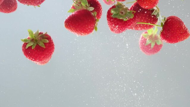Bright juicy strawberry with a splash and bubbles falling into water. Sweet fresh red strawberry berries splashing into transparent water in aquarium, underwater. Slow Motion, close-up