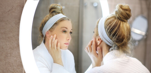 woman looking in the mirror in the bathroom and taking care of her skin.Applying the cream..Magic anti-aging cream.