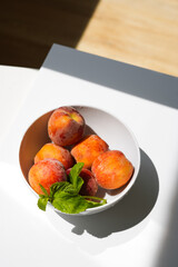 Top view, fragrant fresh appetizing peaches with mint in daylight on white background with shadows