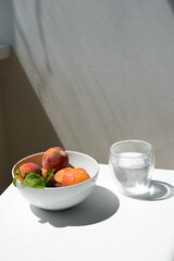 Beautiful ripe peaches in a white city stand on a table in daylight next to a glass of water.