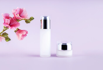glass bottles for cosmetics and flowers on a purple background