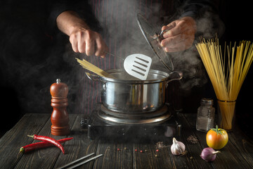 The chef cooks a delicious soup with vegetables and pasta in a hot pot in the kitchen. Delicious hotel food recipe