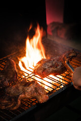 Flame grill BBQ steak meat on charcoal fire stove in dark tone high contrast close up