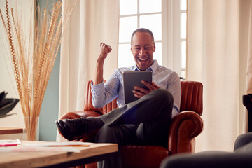 Fototapeta premium Mature Man Or Businessman Working From Home Sitting In Armchair Getting Good News On Digital Tablet