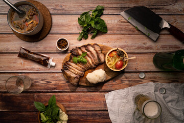 Top view Thai food Grilled Pork jowl serve on round wood plate with spicy papaya salad sticky rice spicy sauce on wood table with drink snack and appetizer meal