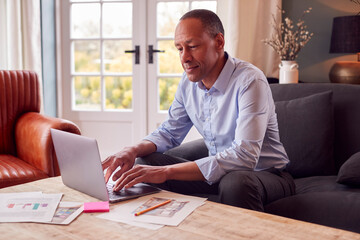 Obraz premium Mature Male Architect Or Interior Designer Working From Home Looking At Designs On Laptop