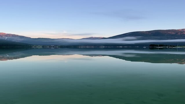 Vertical shot from the shore of rocky hills and blue cloudy sky reflected in Achen lake water