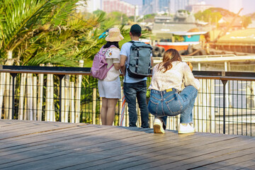 Back view portrait of attractive Asian woman photographer or traveller using a professional mirrorless camera take photo at riverside on sunny day during weekend trip. Attractions and travel concept.