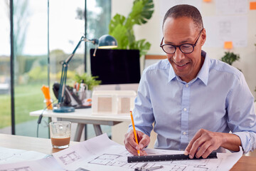 Mature Male Architect Working In Office On Plans For New Building