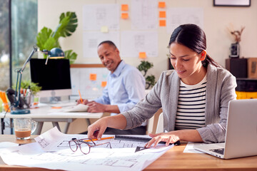 Male And Female Architects Working In Office At Desks On Plans For New Building