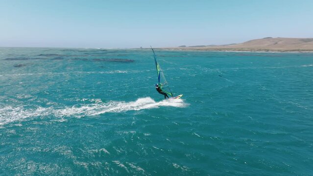 Jul. 2022. California, USA. Drone footage of a wave sailor surrounded by spectacular summer seascape. The rider windsurfing on a crystal clear ocean flat waters by the coast. High quality 4k footage