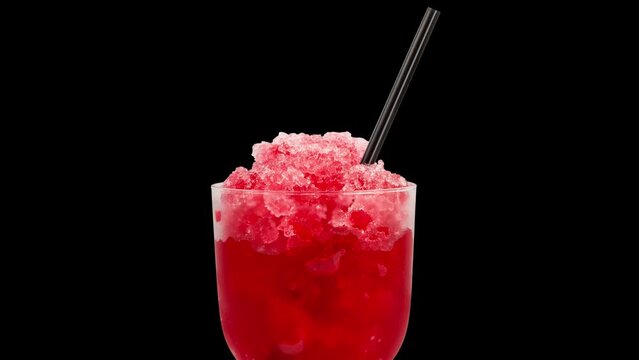 Spanish Granizado or Red Slushie drink with natural juice on black background, close-up. 4K video. Fruit shaved ice in clear glass. Refreshing summer drink. Banner for cafe, restaurant.