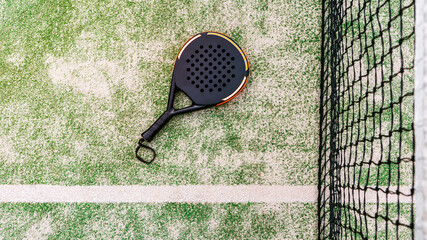 Top view of a black padel racket on a green court grass turf behind the net