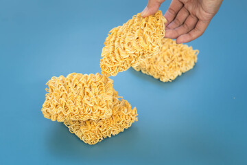 hand holding dry instant noodles on blue background.