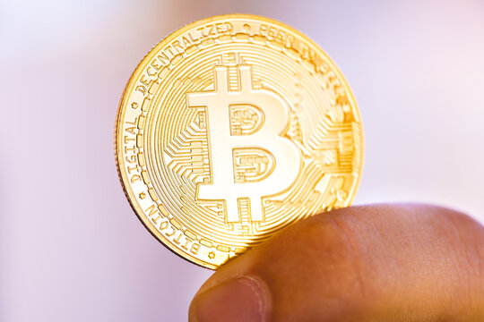 Bitcoin - BTC. Um homem segurando em sua m&atilde;o uma moeda dourada de Bitcoin. Criptomoedas, moeda virtual, forma de pagamento e risco.