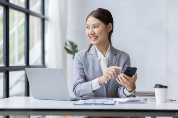 Young Asian Businesswoman uses a mobile phone and works on laptop computer in the modern home office.