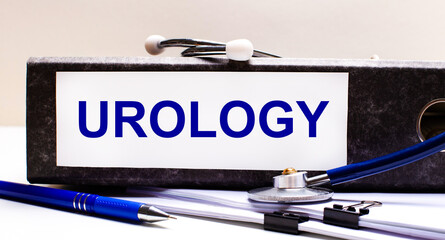 The desktop has a stethoscope, a blue pen, and a gray file folder with the text UROLOGY. Medical...