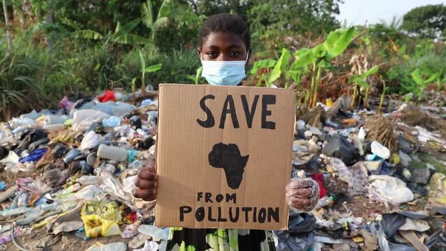 A girl holding a sign with the words "Save Africa From pollution" in front of an illegal open-air landfill.
