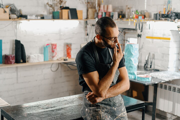 Male artist sculptor artisan smokes a cigarette in the workshop.