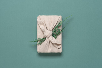 Christmas gift wrapped in fabric with juniper branch, turquoise pastel background. A traditional...