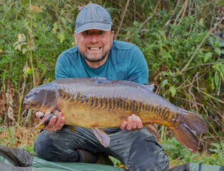 Fisherman holding his catch a carp in his hands with smile on his face.
