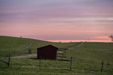 a small building sits under a late sunset in a meadow one winter evening