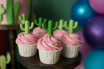 Cupcakes with pink cream decorated with cacti. Summer sweet birthday table.