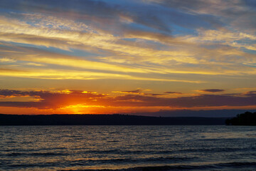 Fototapeta na wymiar sunset over the lake, bright sun reflected in the waves, glare on the water, beautiful summer landscape