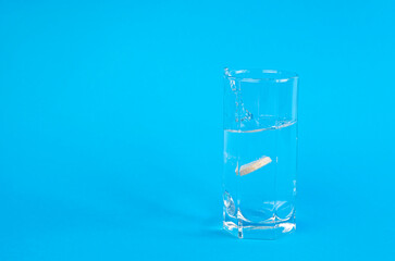 Glass of water and splashes of water. An effervescent tablet that dissolves in water on a blue background.