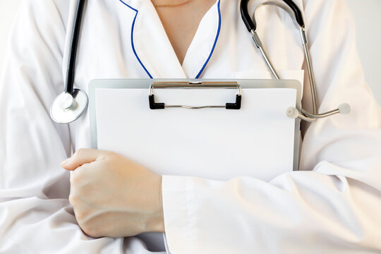 A woman doctor in a white coat holds a clipboard in her hands. Close-up photo.
