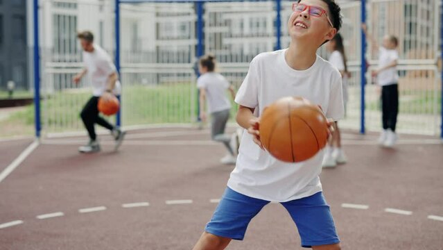 Asian boy in glasses trainings with ball on basketball court. schoolboy catching the ball and improve his skills in basketball.