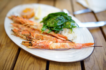 Big grilles shrimps on skewers with rice and spinach on a white plate in restaurant in Cyprus. Mediterranean cuisine