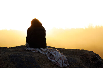 Fototapeta na wymiar Silhouette woman sits on a rock against the backdrop of a foggy dawn